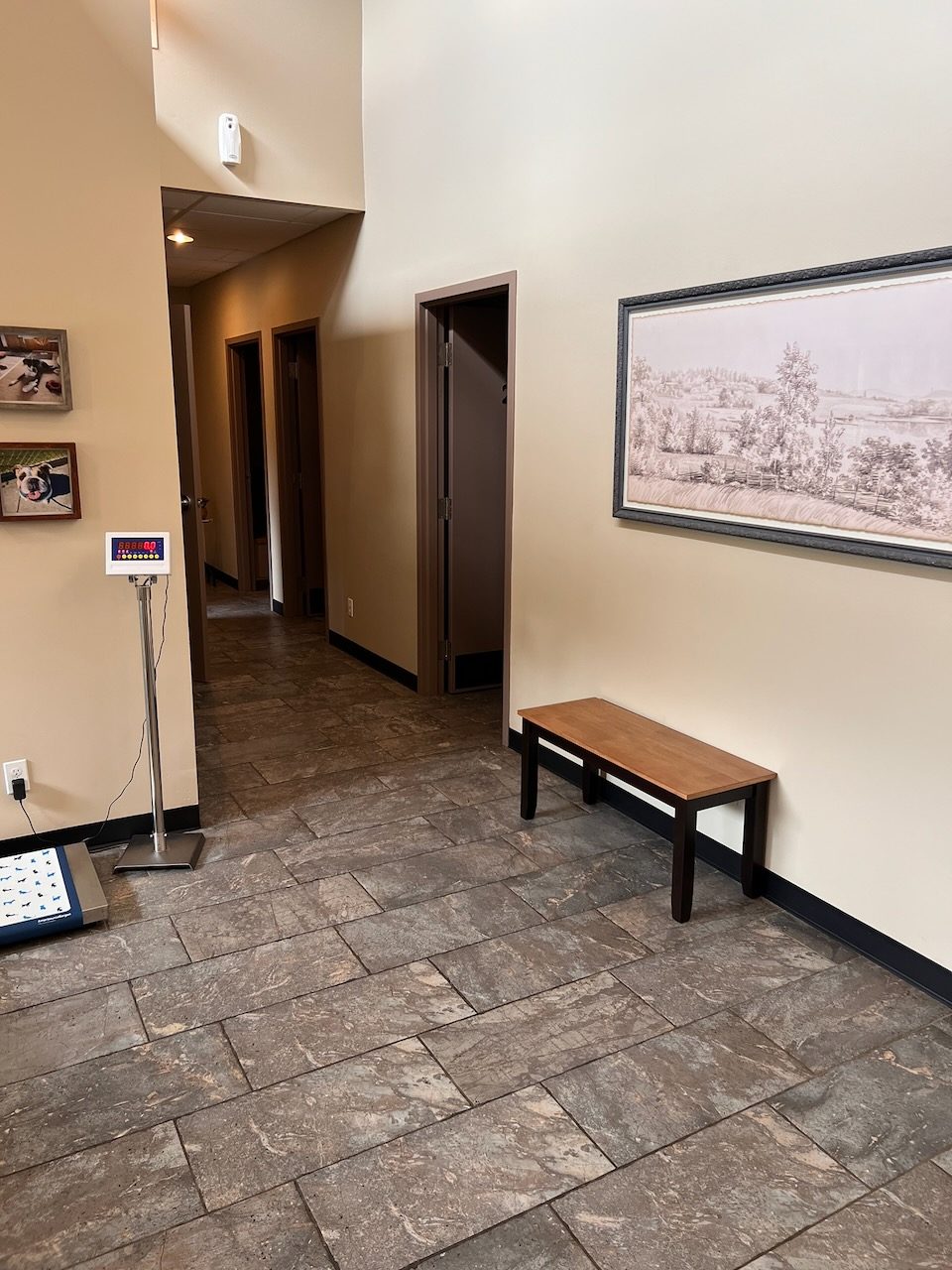 A hallway past the walk-on scale, with a wooden bench and a framed pastoral print