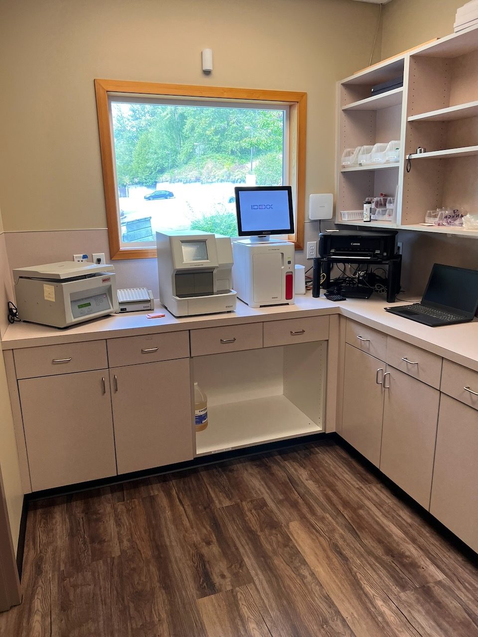 Lab analyzers and a monitor on a counter beneath a window looking out on trees