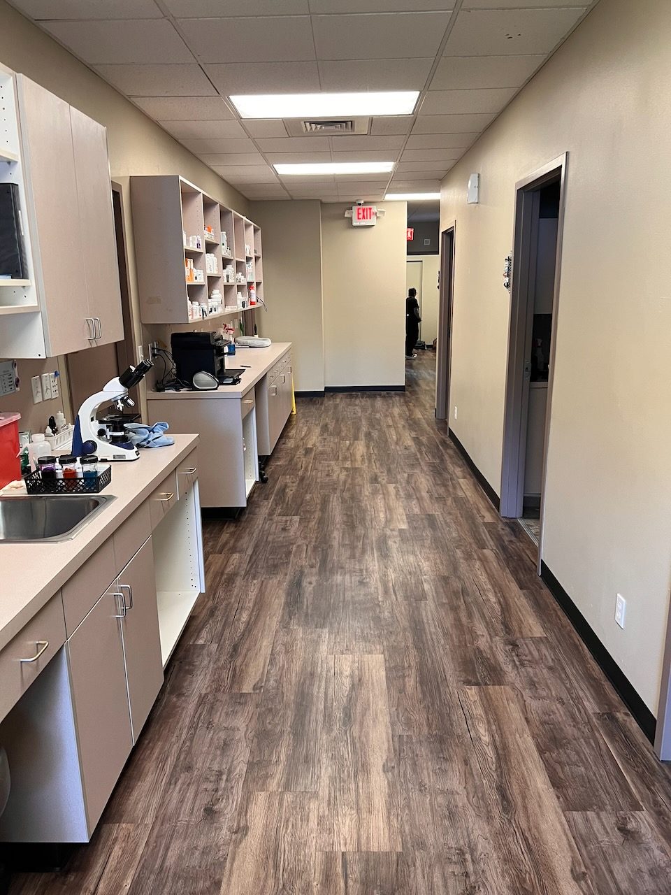A long corridor lined with lab counters, a microscope, and pharmacy shelving
