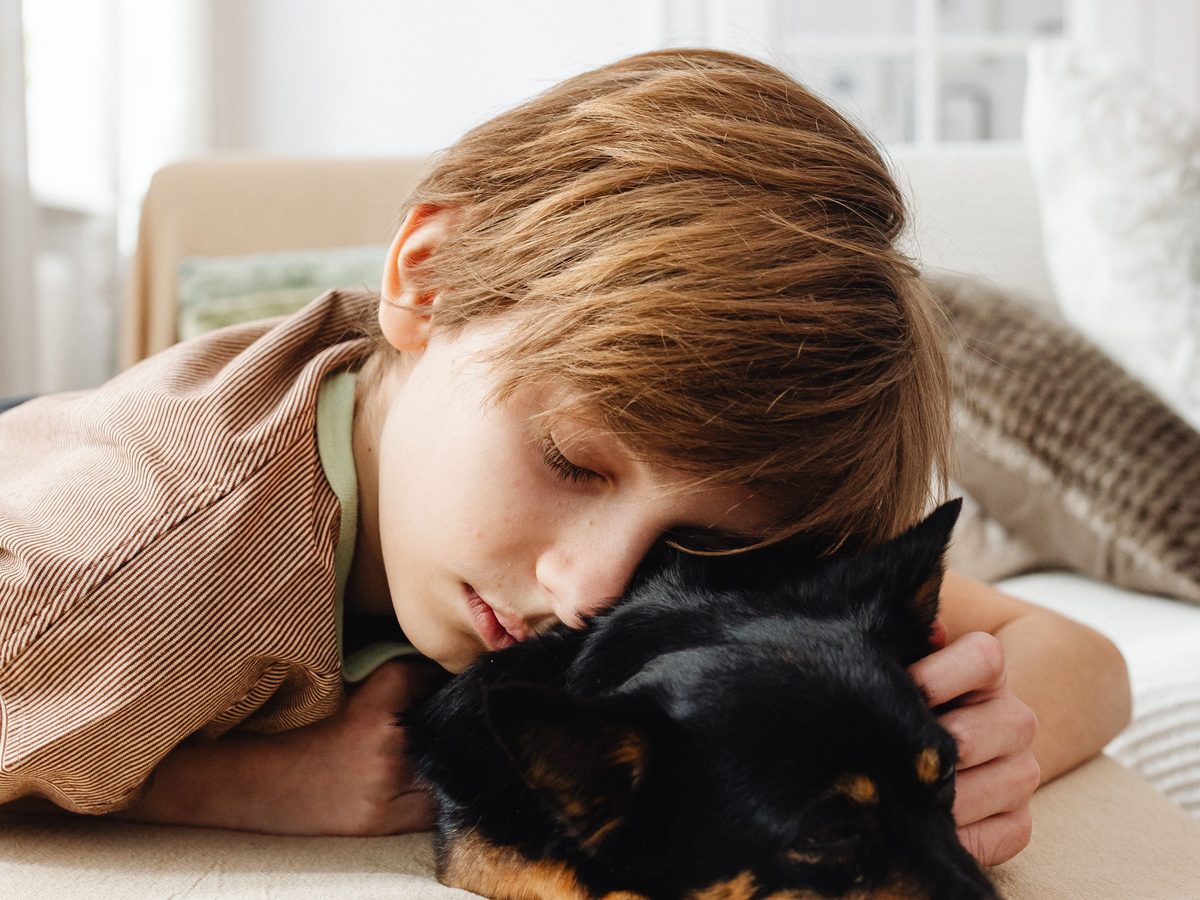 A boy resting his cheek against his small black dog on a sofa